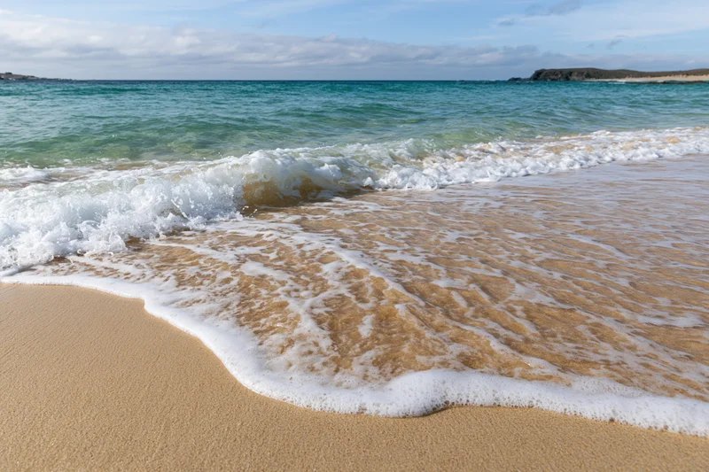 Waves breaking on sandy beach with foam at shoreline under blue sky
