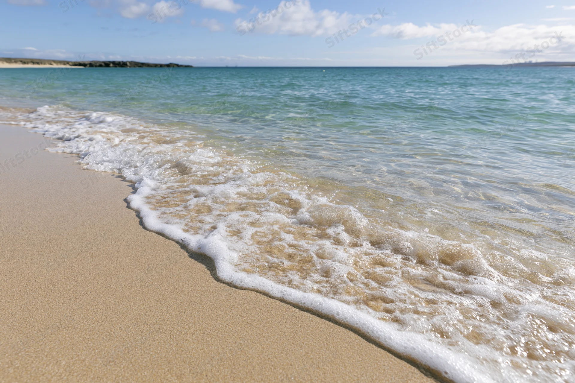 Gentle waves rolling onto sandy beach under clear sky
