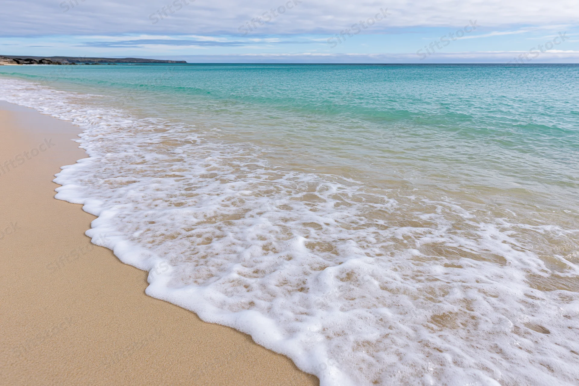 Gentle waves with white foam rolling onto sandy beach under clear sky
