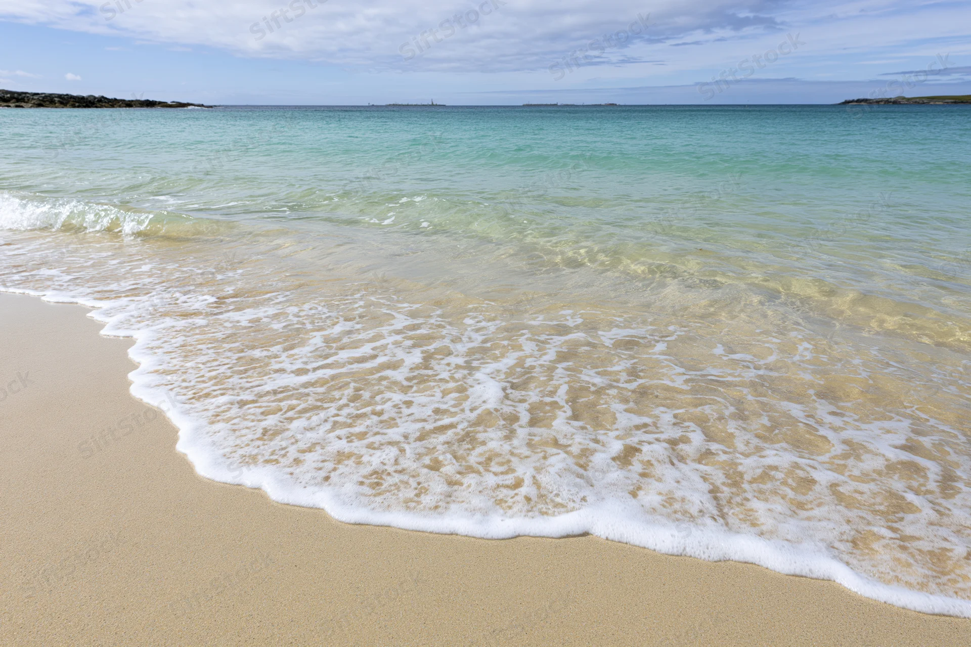 Gentle waves rolling onto a sandy beach under a partly cloudy sky