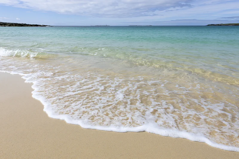 Gentle waves rolling onto a sandy beach under a partly cloudy sky