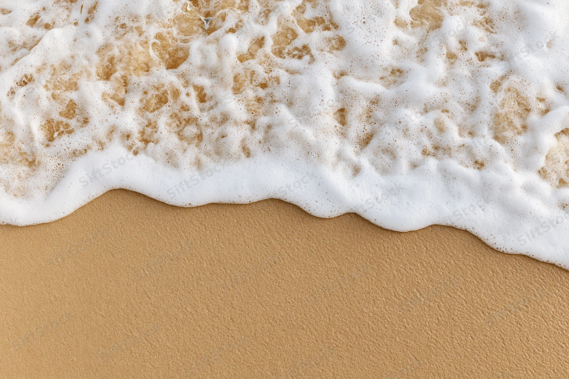 White foamy wave washing over golden sand at the beach shoreline
