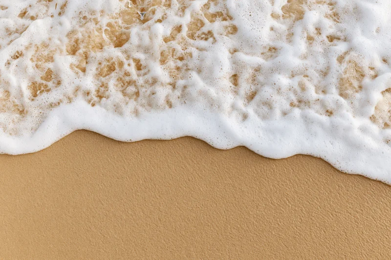 White foamy wave washing over golden sand at the beach shoreline
