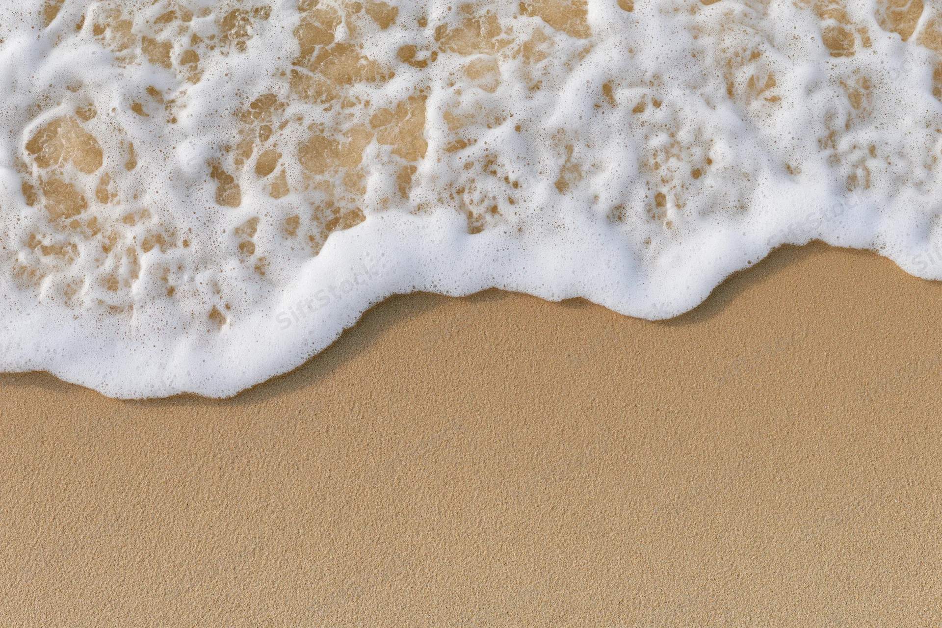 White foam from a wave washing over golden sand at the shoreline