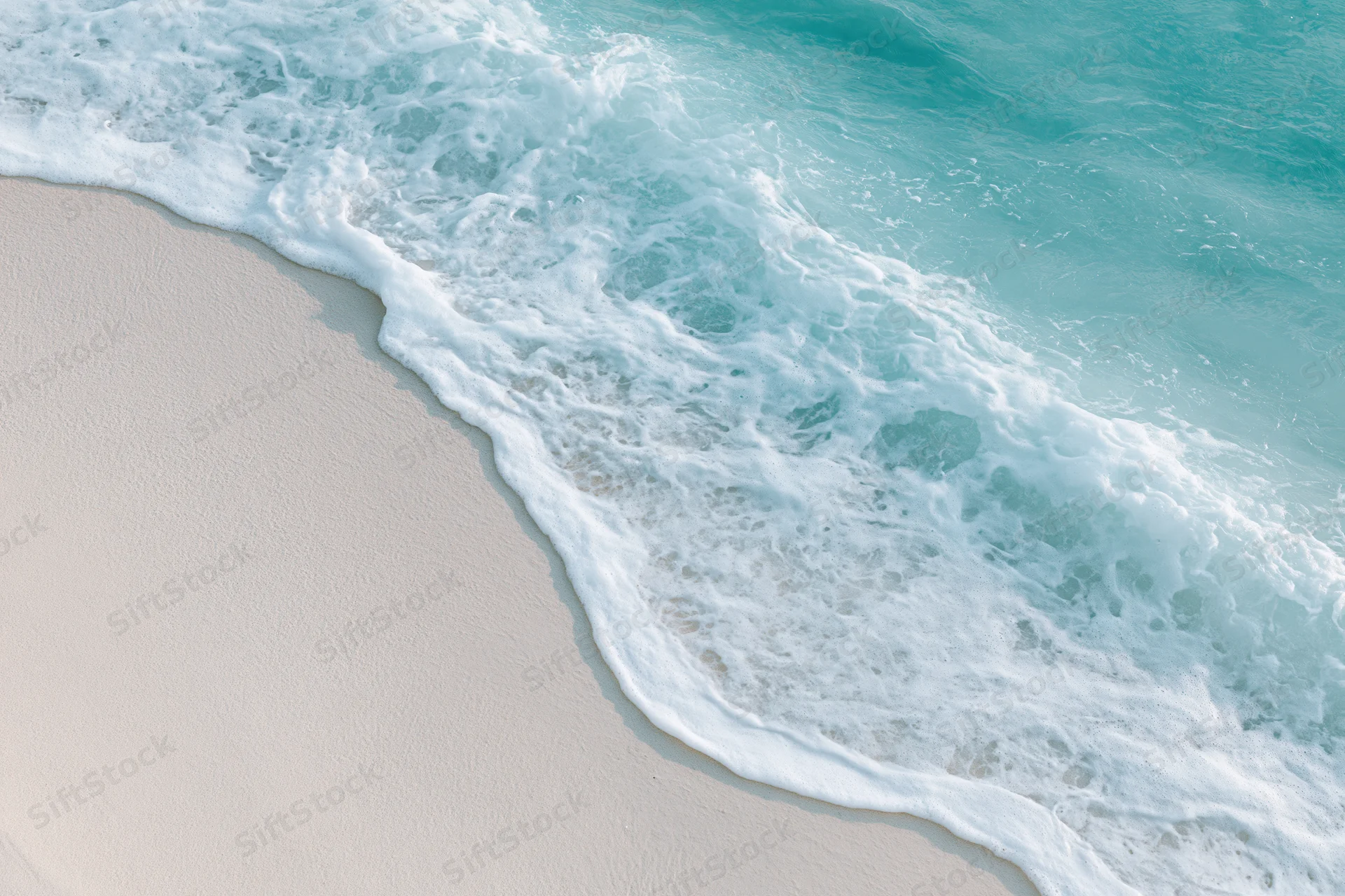 Turquoise ocean wave with white foam washing onto light sand beach