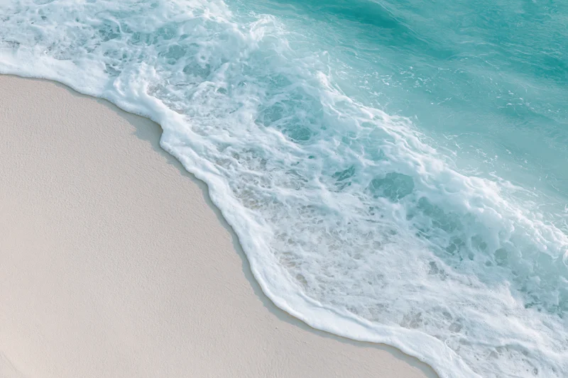 Turquoise ocean wave with white foam washing onto light sand beach
