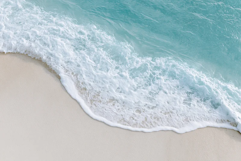 Turquoise ocean wave with white foam washing onto light sand beach