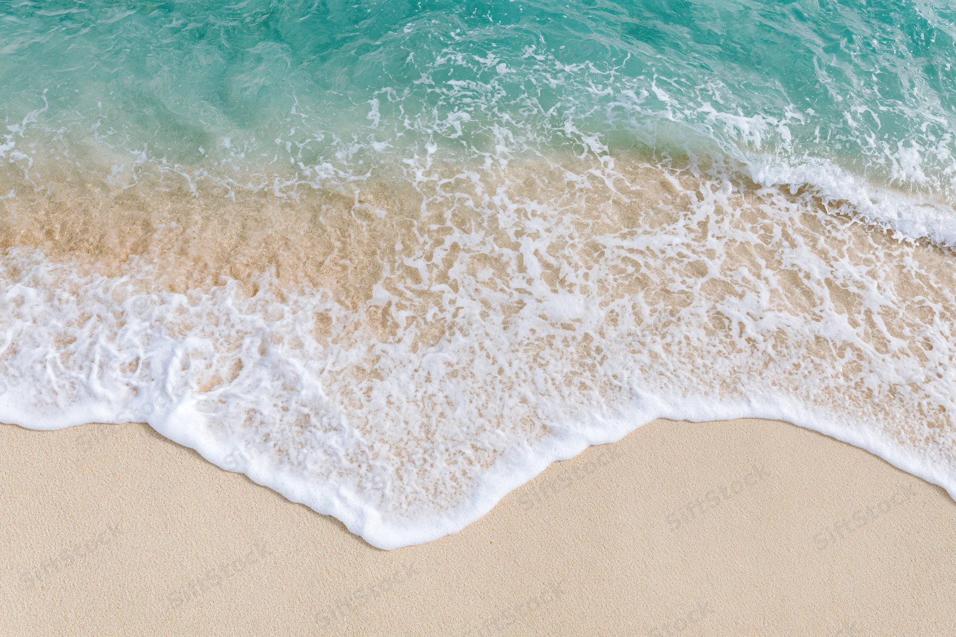 Gentle wave with white foam washing over sandy beach