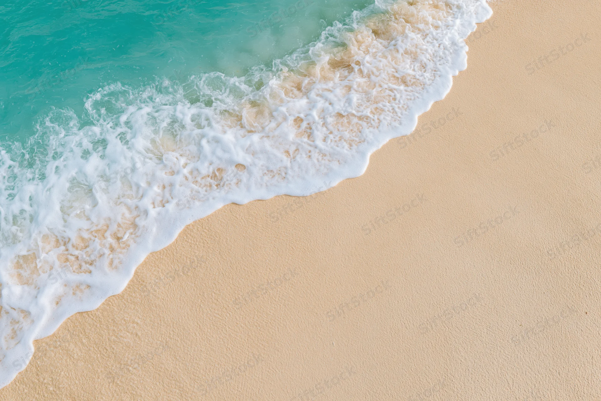 Turquoise ocean wave with white foam washing onto sandy beach