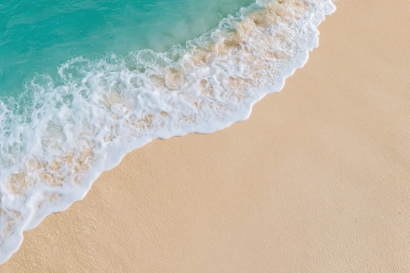 Turquoise ocean wave with white foam washing onto sandy beach