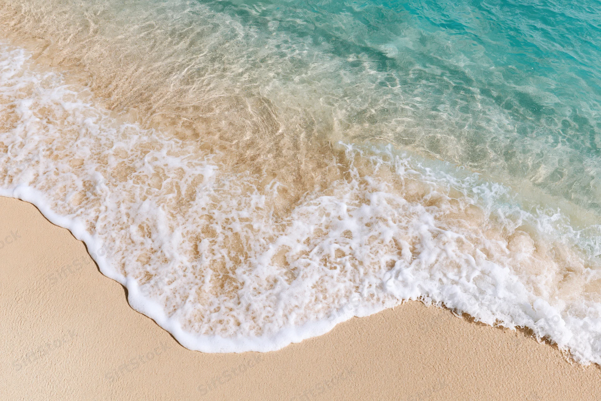 Gentle wave with white foam washing over golden sand at the shoreline