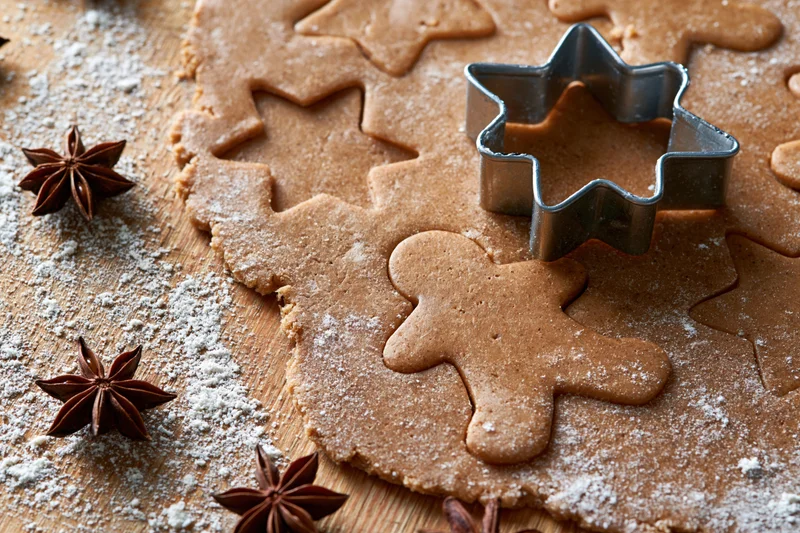Gingerbread dough being cut into shapes on a floured wooden board with star anise and a metal cutter