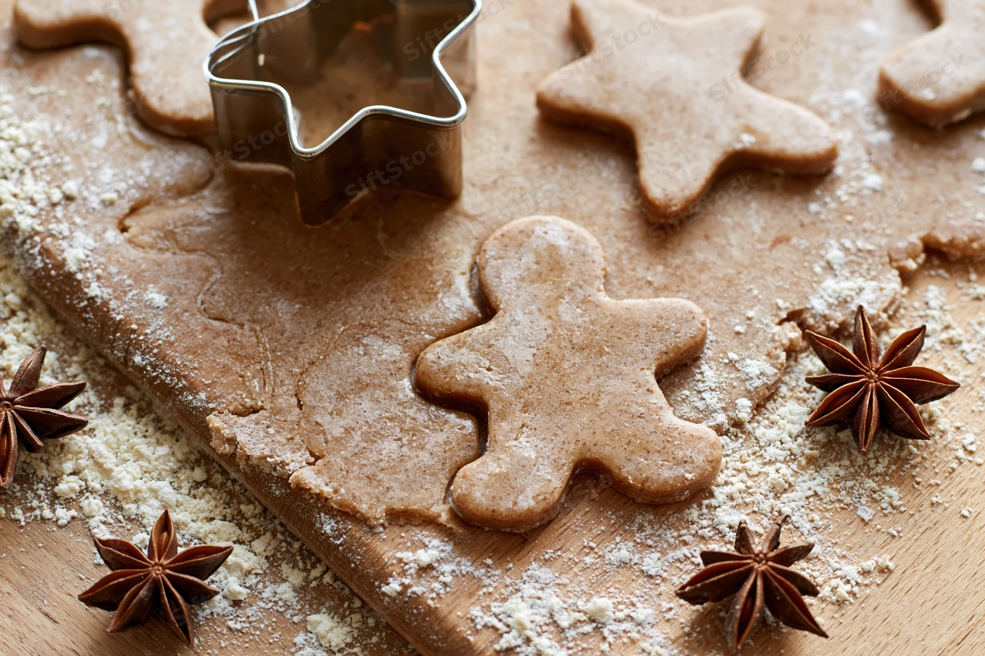 Gingerbread dough cut into shapes on a wooden board with star anise and flour scattered around