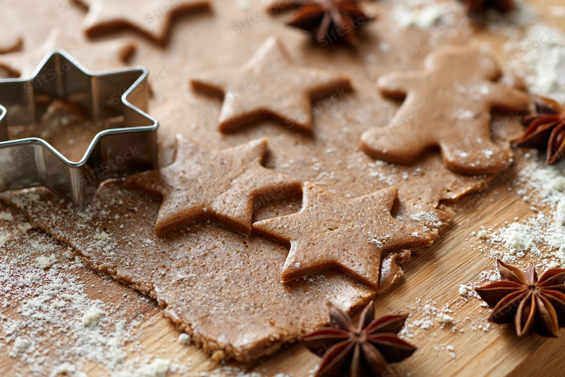 Gingerbread dough cut into star and gingerbreadman shapes on a wooden cutting board with flour and star anise scattered around