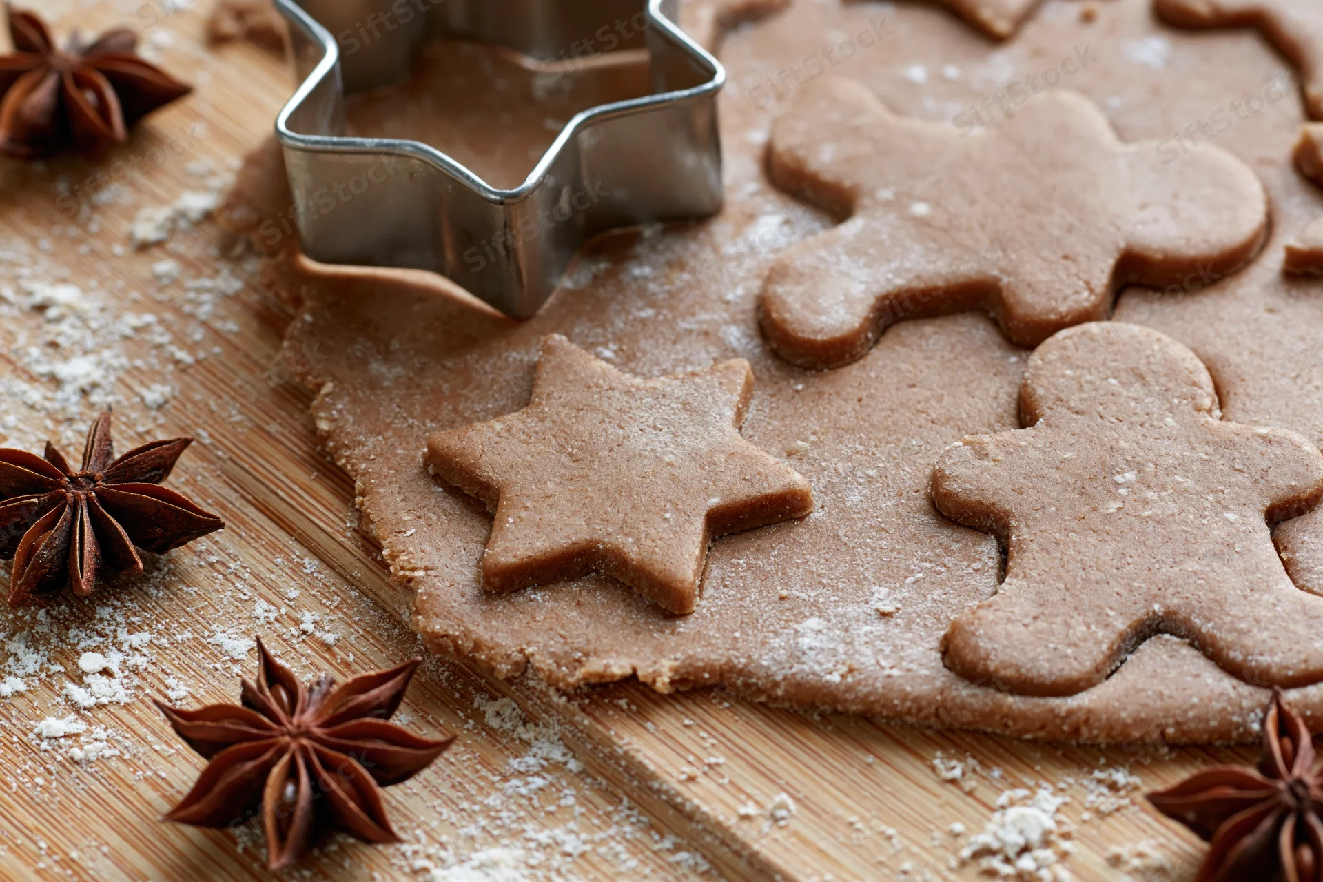 Gingerbread dough cut into star and gingerbreadman shapes on a wooden board with star anise and flour scattered around