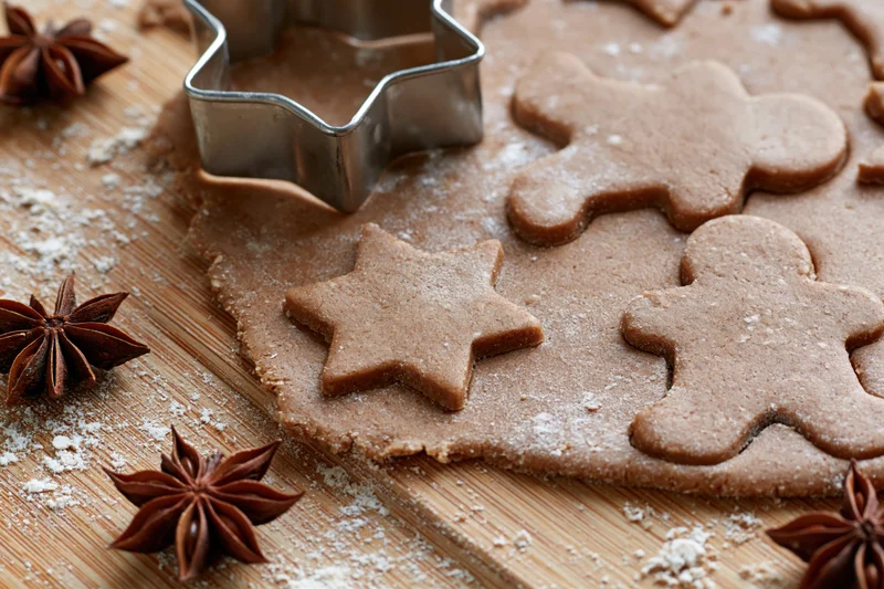 Gingerbread dough cut into star and gingerbreadman shapes on a wooden board with star anise and flour scattered around