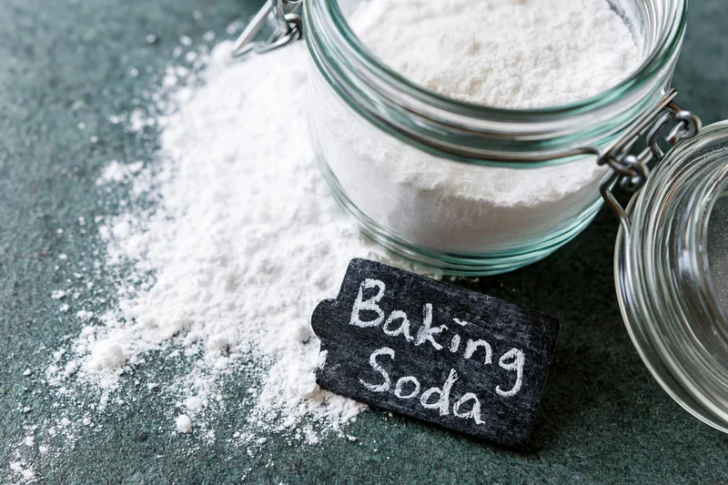 Baking soda powder spilled from a glass jar on a dark countertop with a chalk label reading baking soda