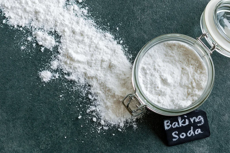 Baking soda powder spilled beside a glass jar with a chalkboard label on a dark countertop