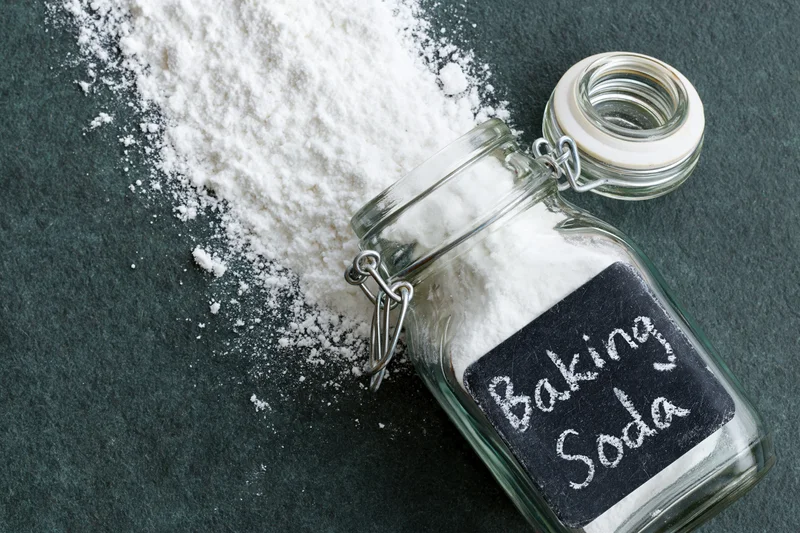 Glass jar labeled baking soda with spilled white powder on dark countertop