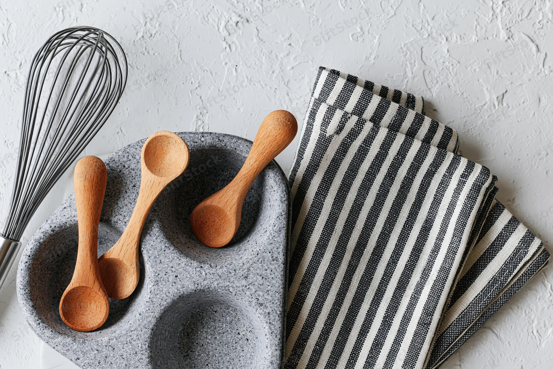 Wooden spoons and whisk arranged on a gray ceramic tray with a striped napkin on a white textured surface