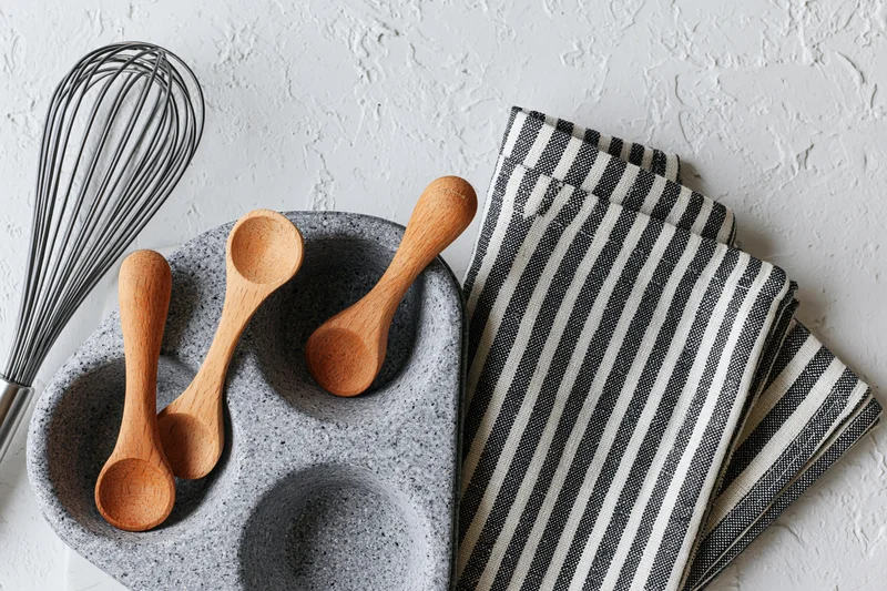 Wooden spoons and whisk arranged on a gray ceramic tray with a striped napkin on a white textured surface