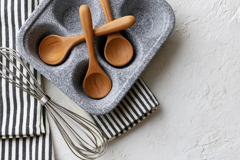 Wooden spoons and a whisk arranged in a gray dish on a striped cloth over a white textured surface
