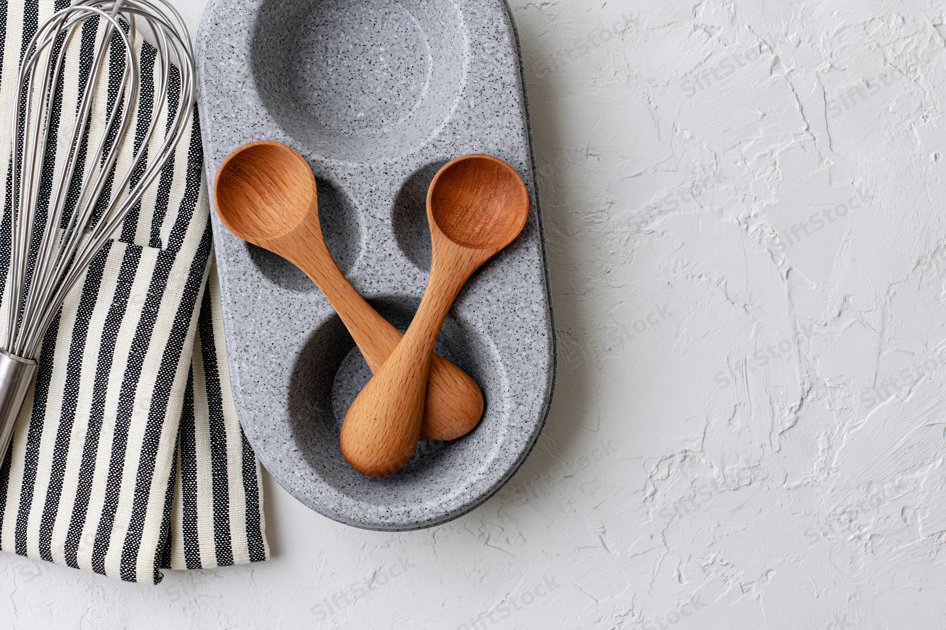 Wooden spoons and whisk arranged on a striped cloth and ceramic tray on a white textured surface