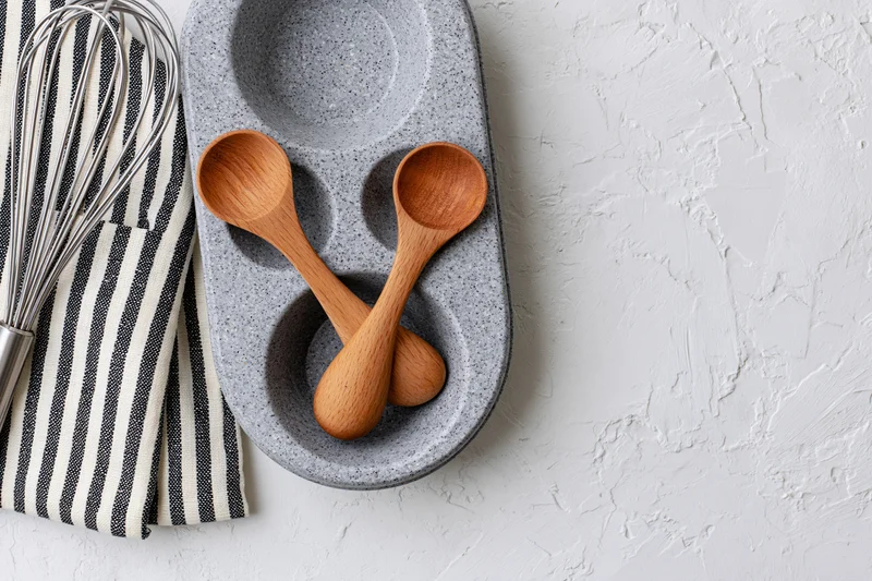 Wooden spoons and whisk arranged on a striped cloth and ceramic tray on a white textured surface