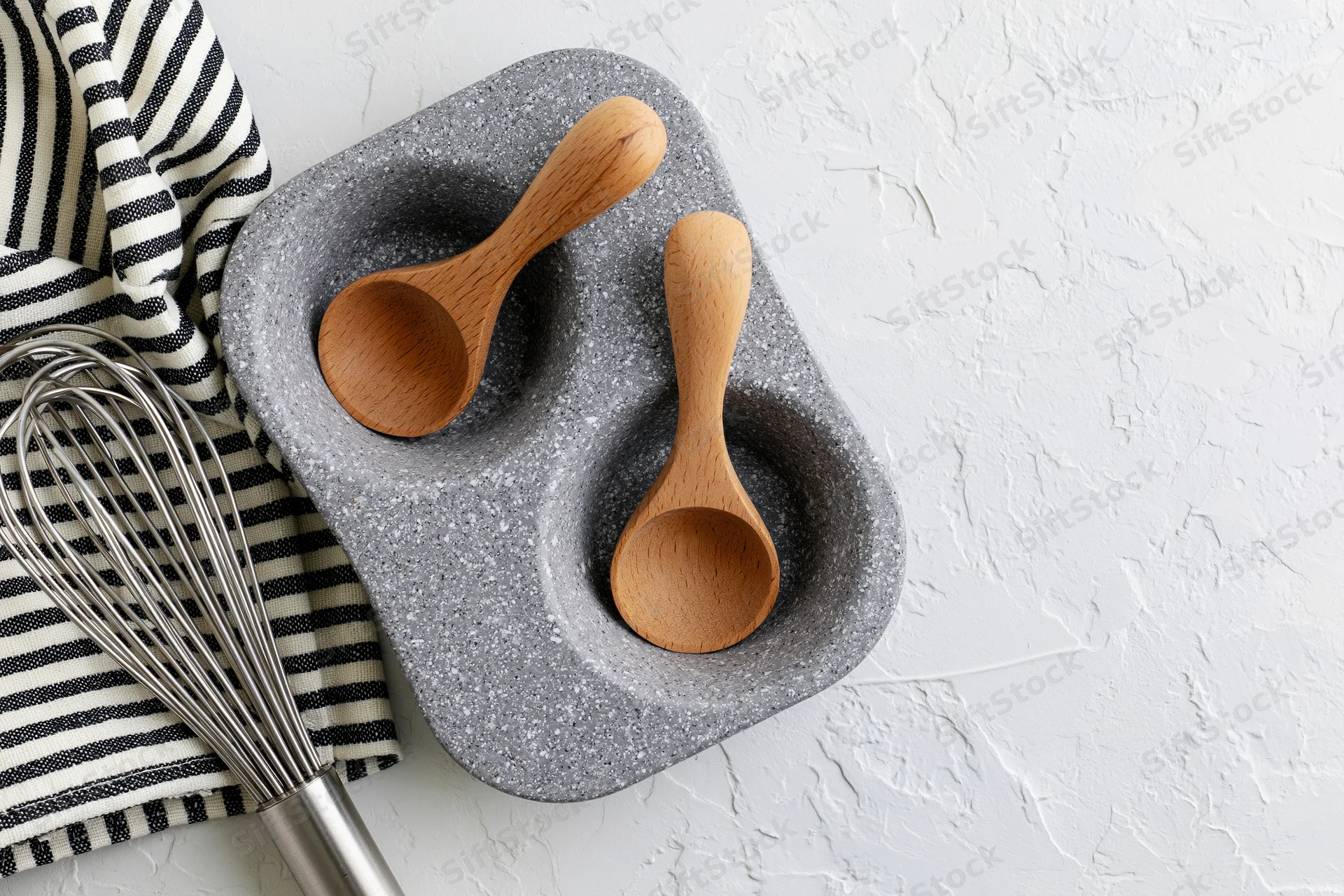 Wooden spoons and whisk arranged on a gray speckled tray with striped cloth on white surface