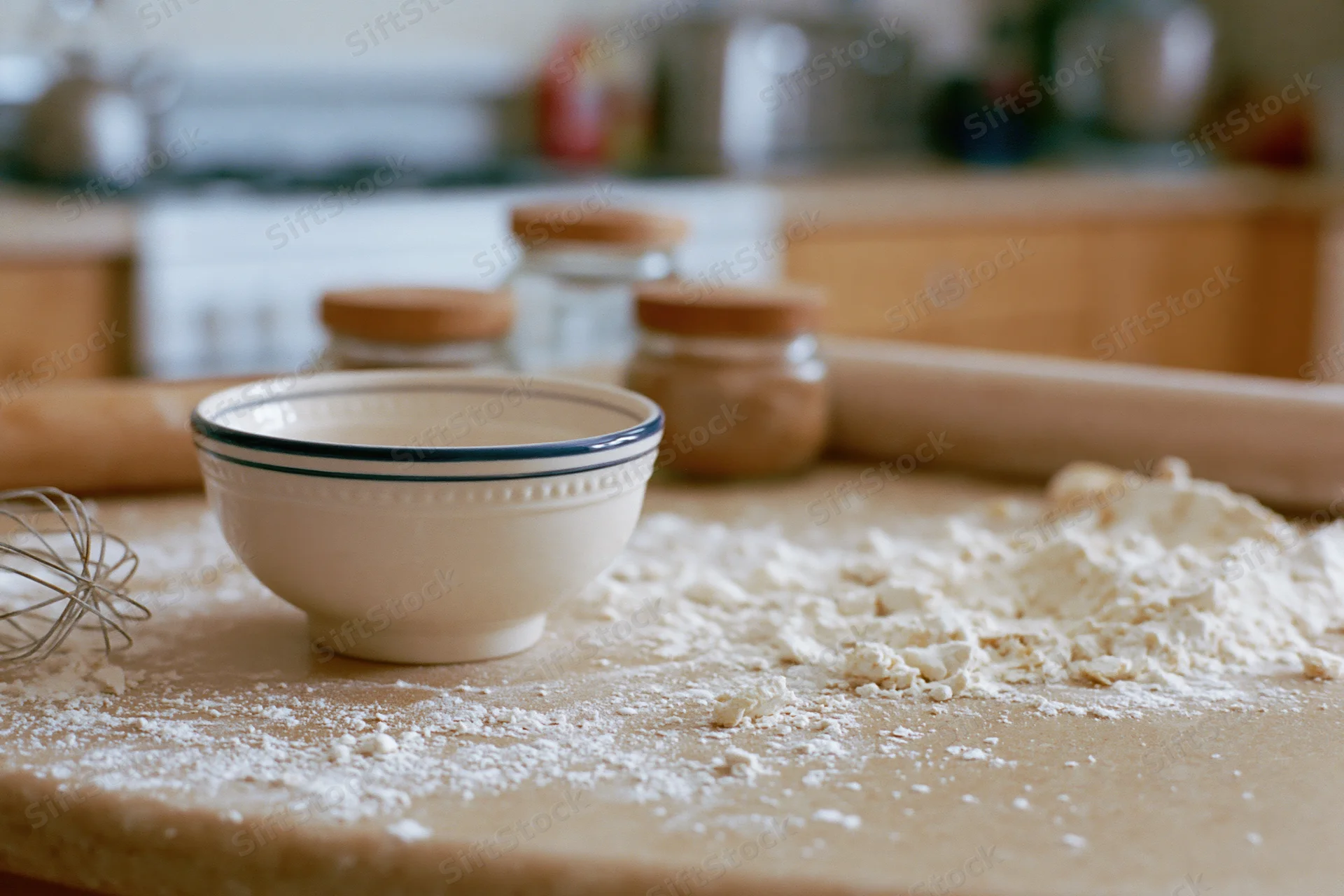 Flour scattered on a wooden countertop with a ceramic bowl and baking tools in a kitchen