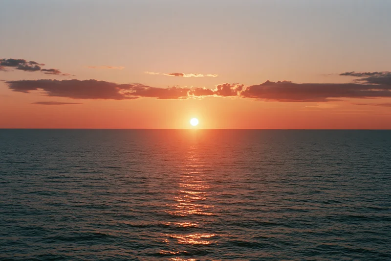 Sunset over the ocean with sun at horizon casting warm reflection on water surface
