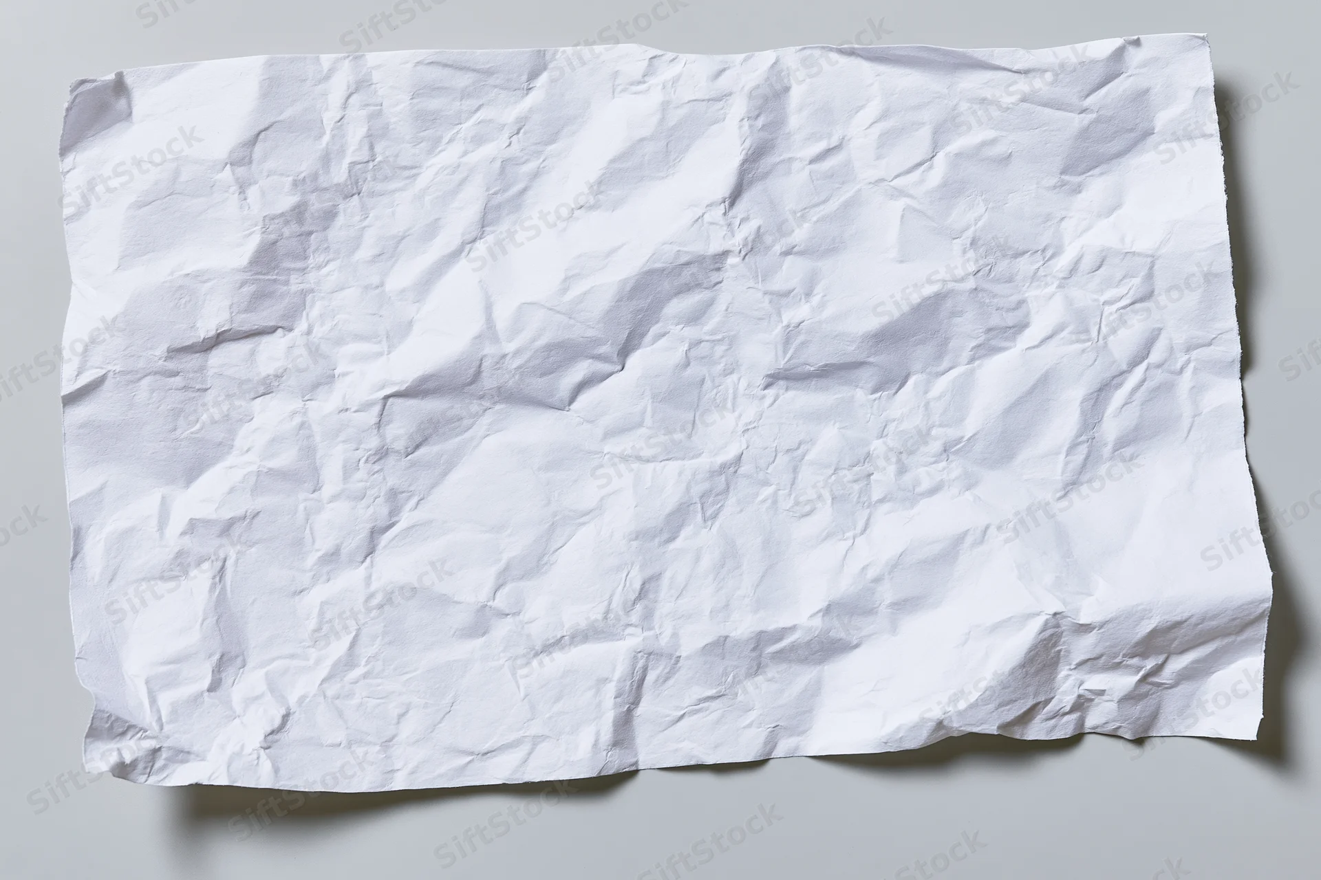Crumpled white paper sheet lying flat on a gray surface with soft shadows and copyspace