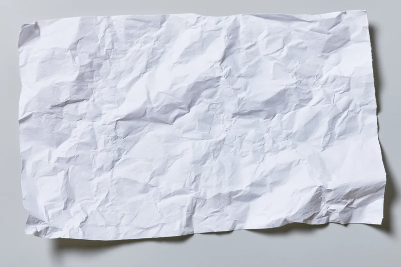 Crumpled white paper sheet lying flat on a gray surface with soft shadows and copyspace