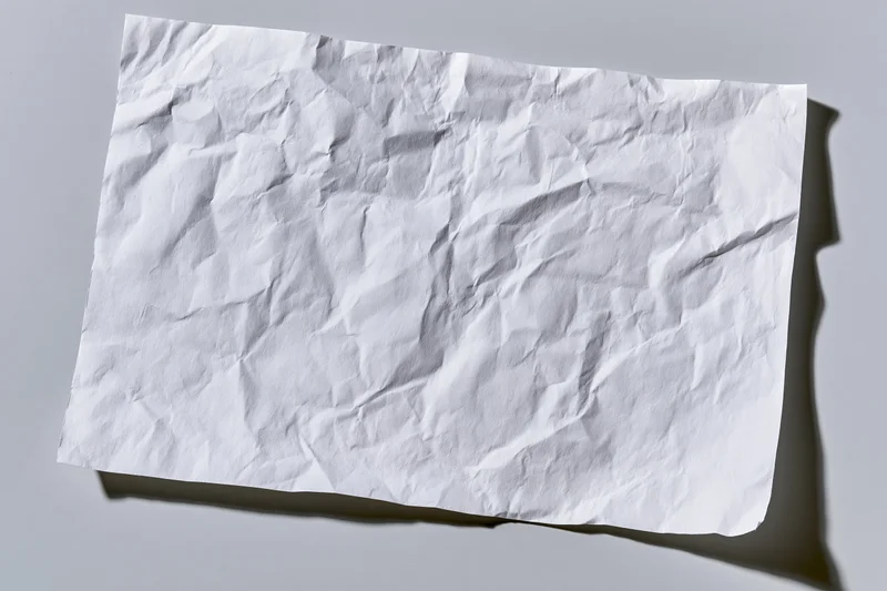 Crumpled white paper sheet lying flat on gray surface with soft shadow