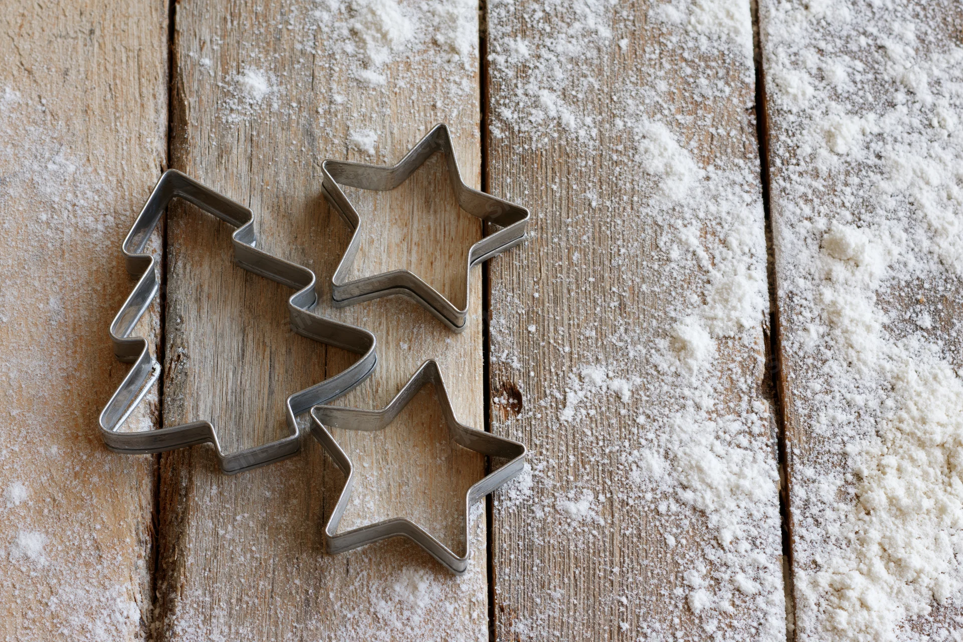 Star and tree shaped cookie cutters on a flour-dusted wooden table