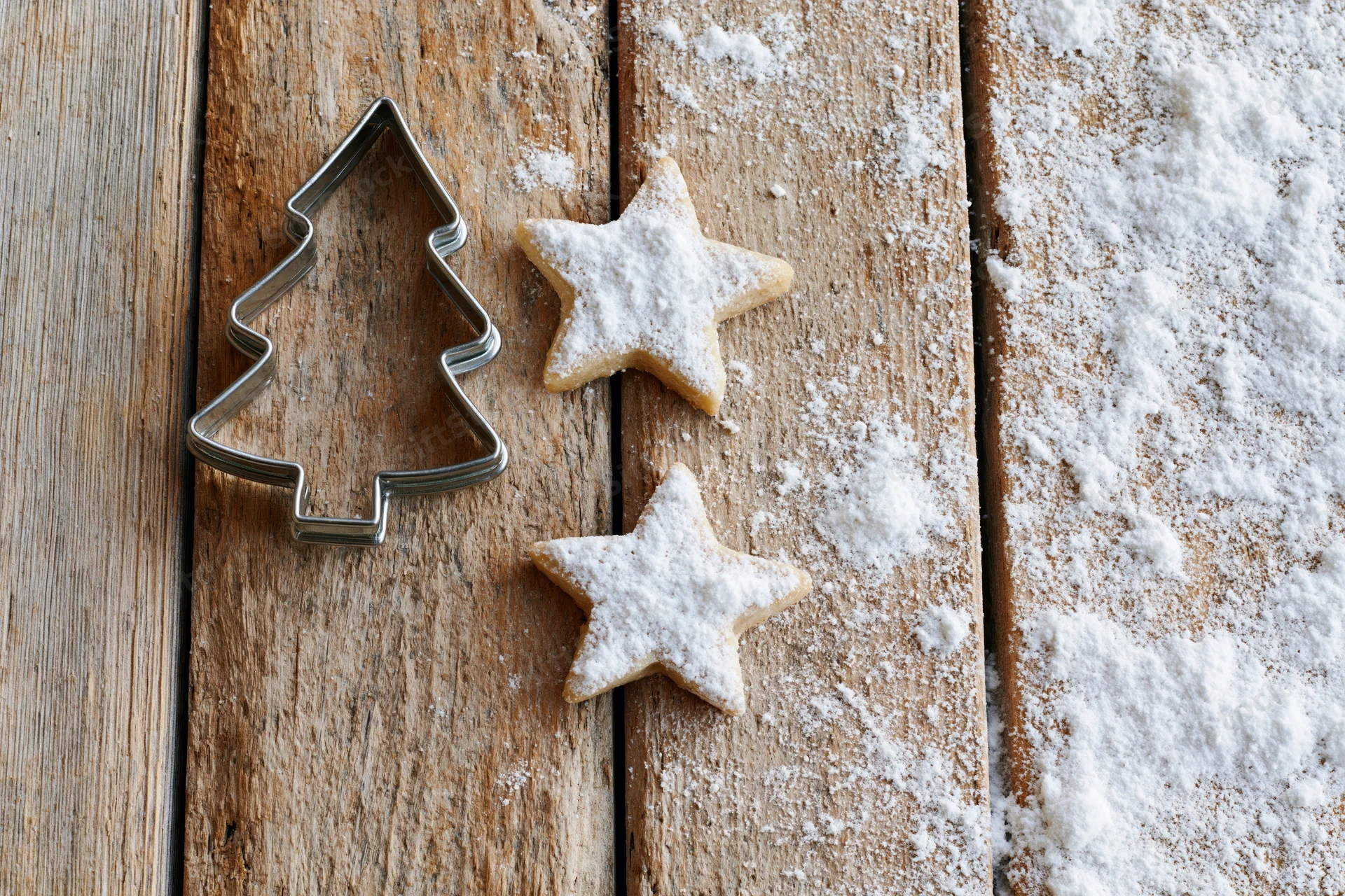 Star-shaped cookies dusted with sugar next to a tree-shaped cookie cutter on a wooden table