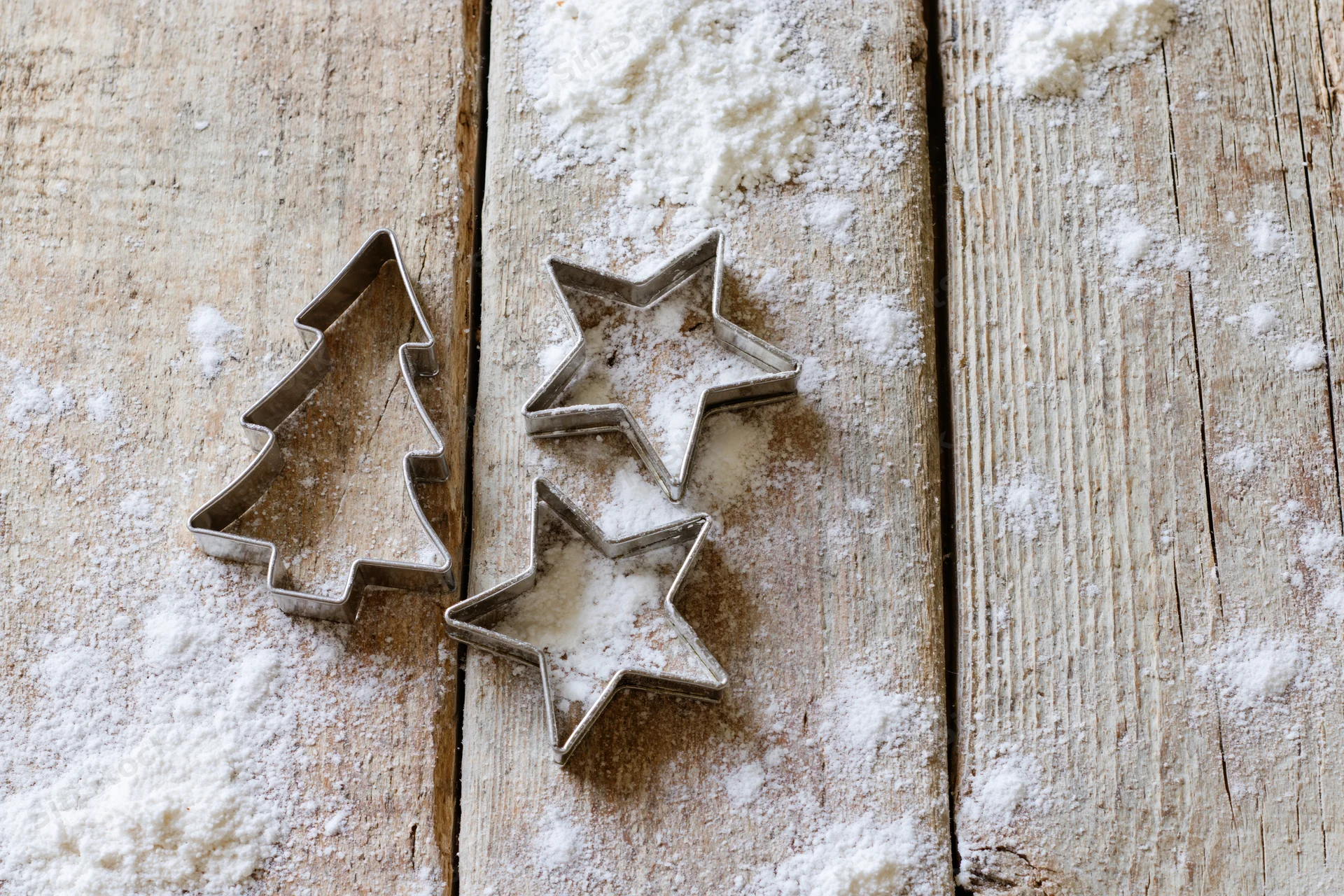 Christmas cookie cutters shaped like stars and a tree on a flour-dusted wooden table