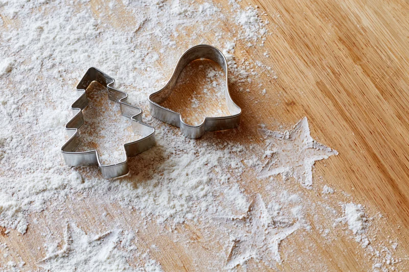 Christmas cookie cutters resting on flour-dusted wooden table with star shapes imprinted in powder