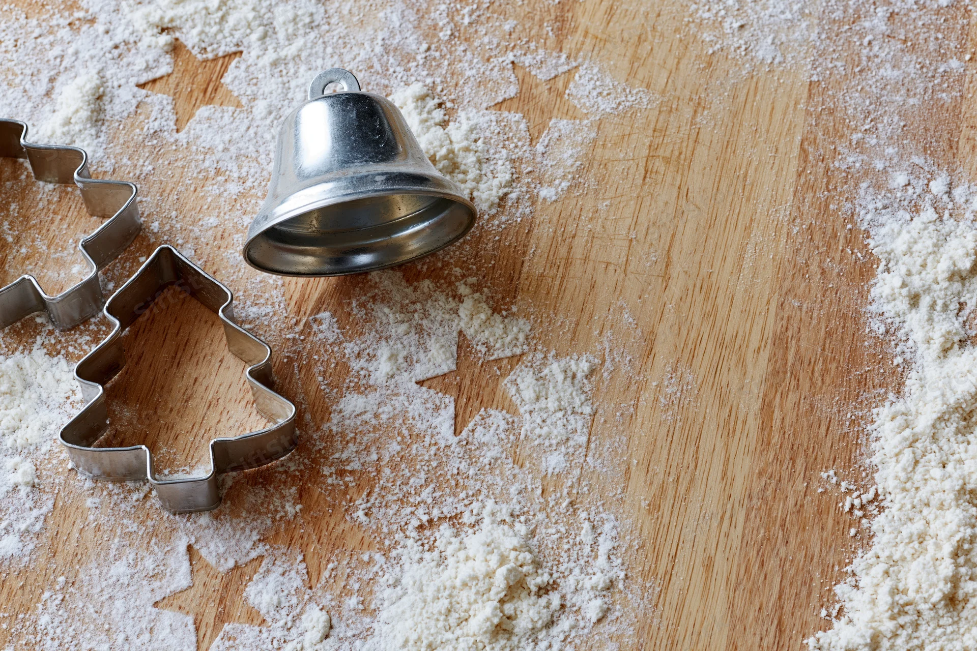 Christmas cookie cutters and a bell on a floured wooden table