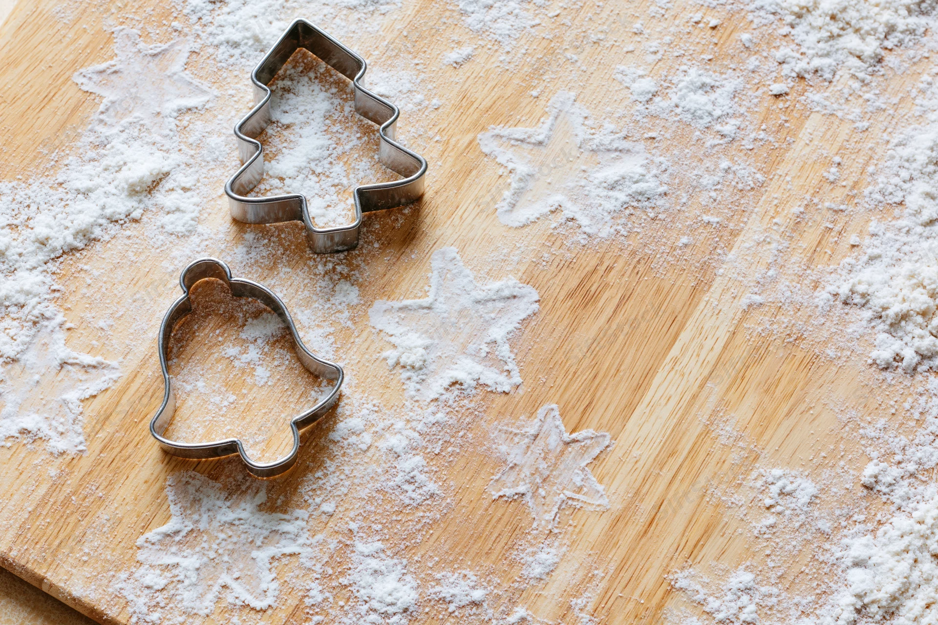 Christmas cookie cutters shaped like tree and bell on a floured wooden board with star patterns