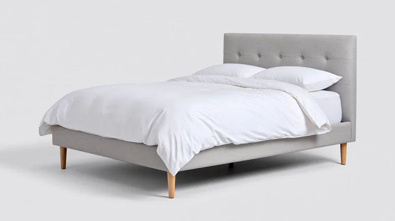 Modern upholstered bed with white bedding and wooden legs on plain background