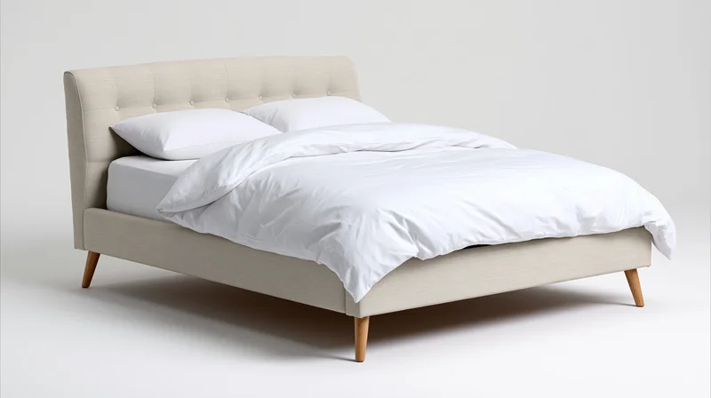 Beige tufted bed with white bedding on wooden legs against white background
