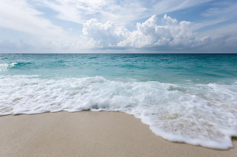 Gentle waves rolling onto a sandy beach under a bright blue sky with scattered clouds