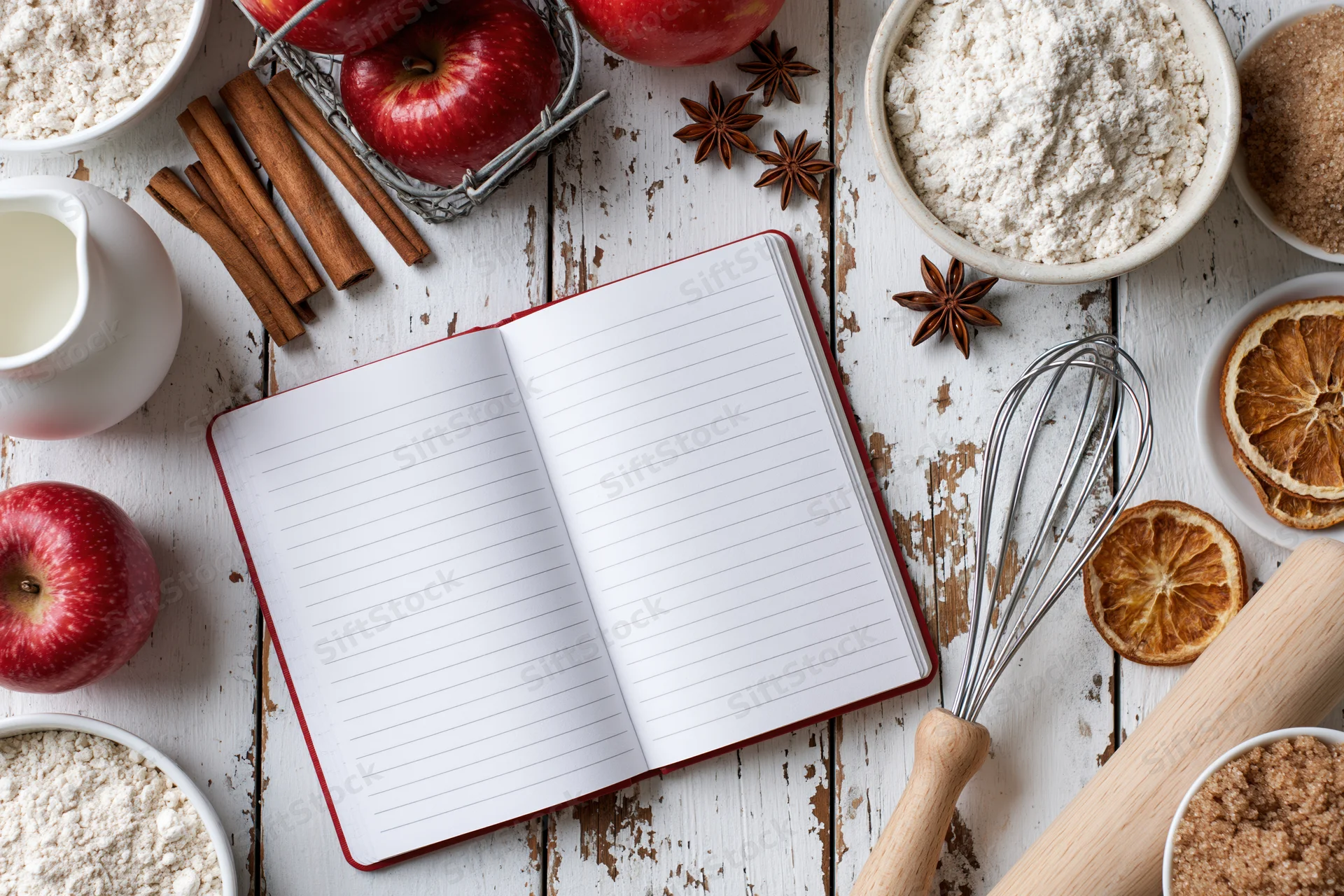 Open notebook with baking ingredients arranged on a rustic white wooden table