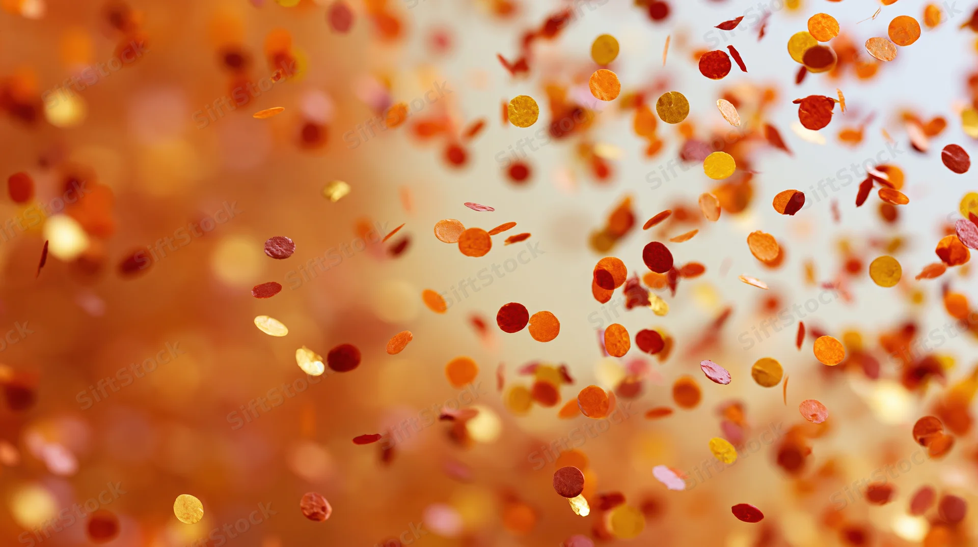 Orange and gold confetti floating in the air against a soft blurred background