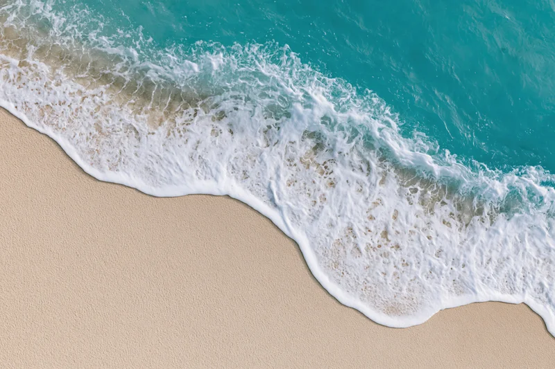 Wave breaking on sandy beach with white foam and turquoise water