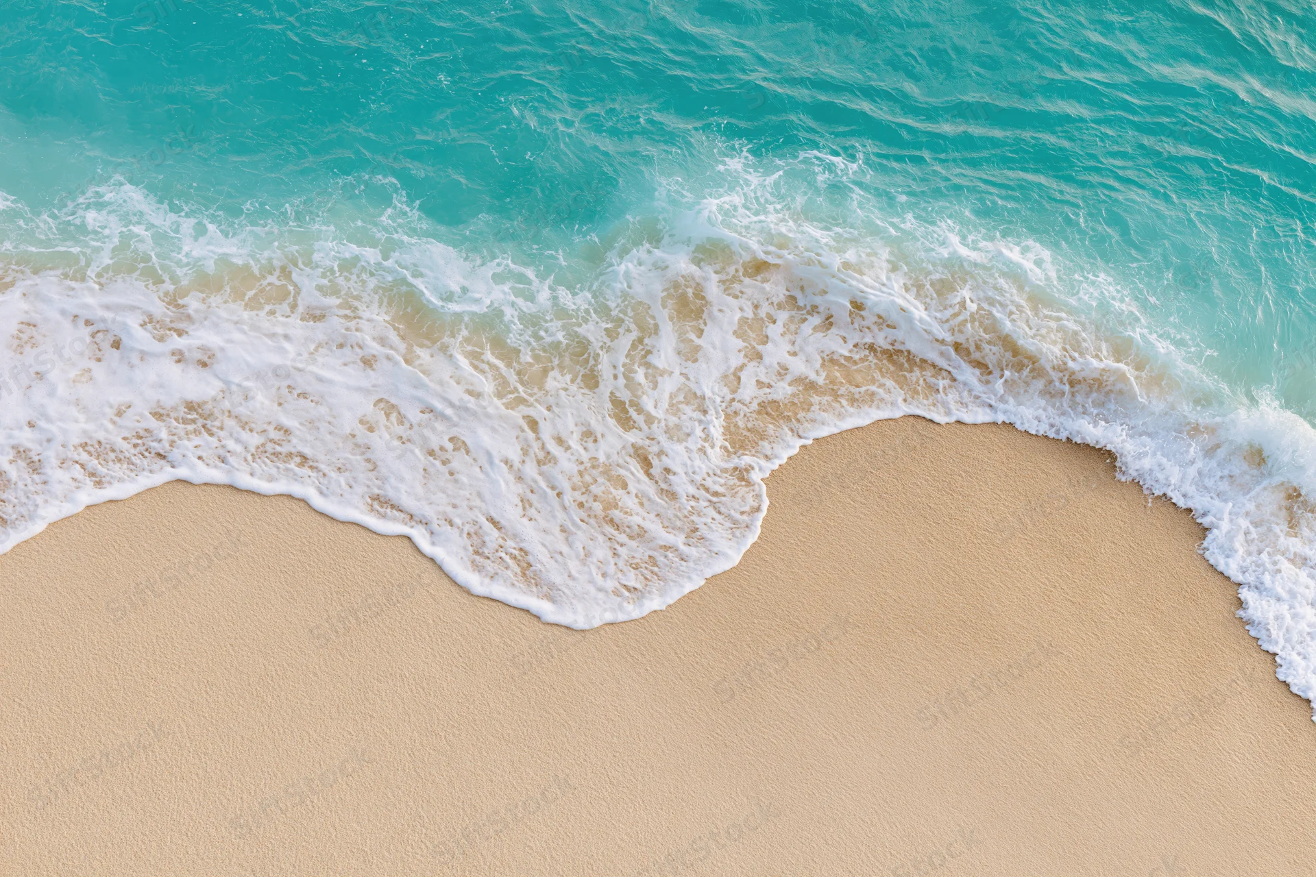 Turquoise waves breaking onto a sandy beach from above