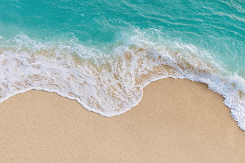 Turquoise waves breaking onto a sandy beach from above
