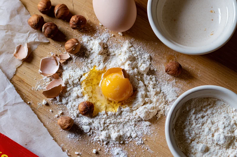 Cracked egg with flour and hazelnuts on wooden surface for baking preparation