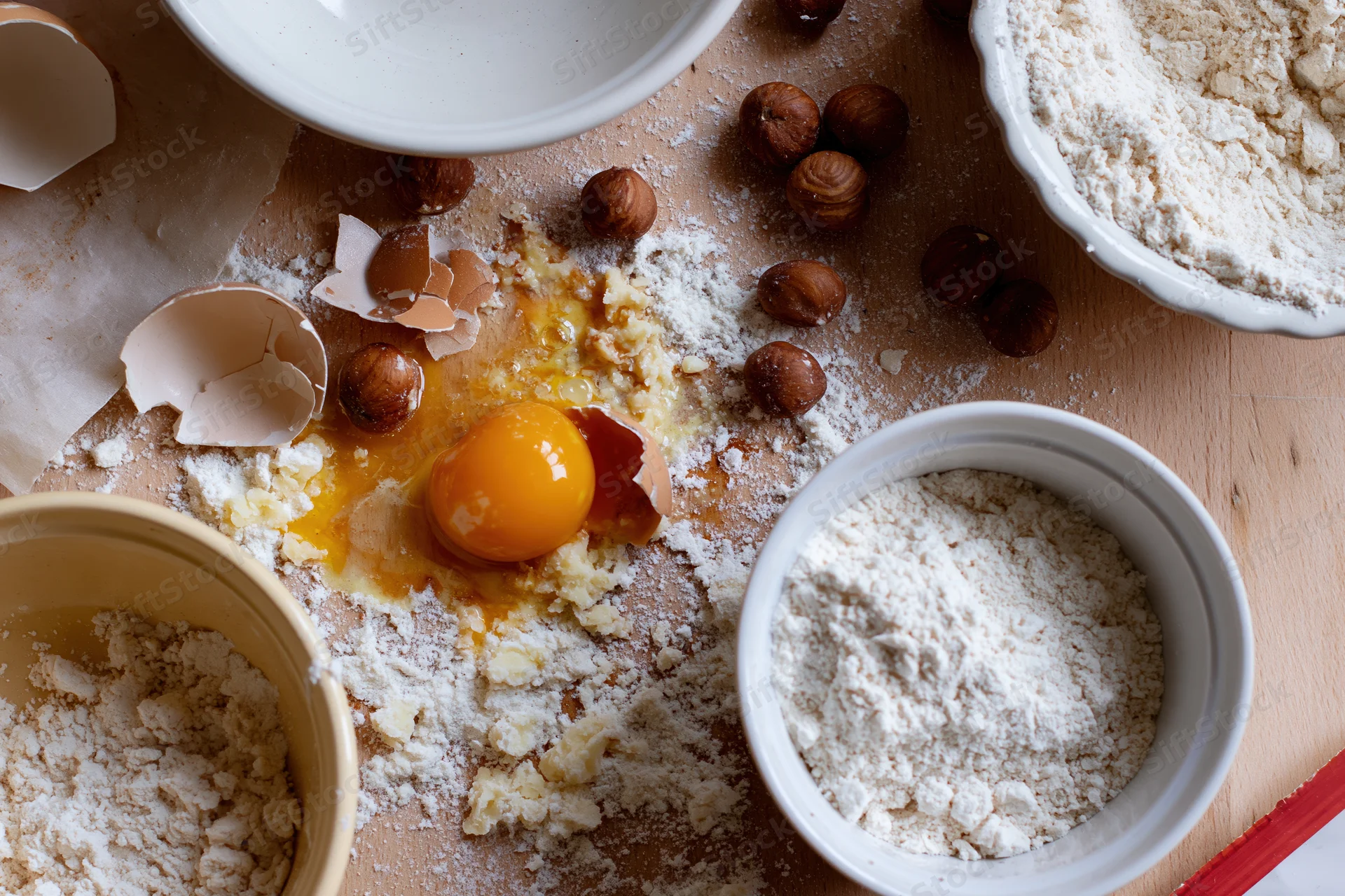 Cracked egg with flour and hazelnuts on wooden countertop during baking preparation